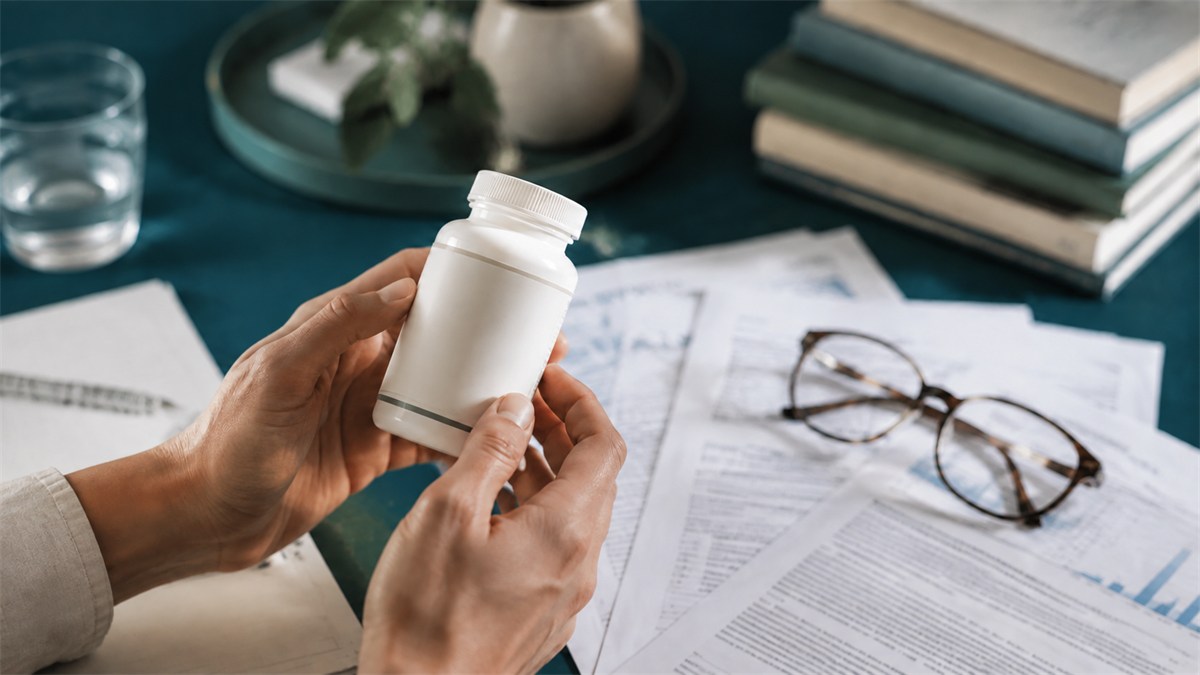 Hands inspect a supplement bottle beside research papers.